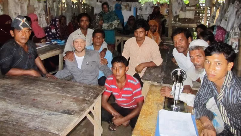 Cameron Conaway during his investigative journalism fieldwork, sitting with a group of people in a workshop in Bangladesh