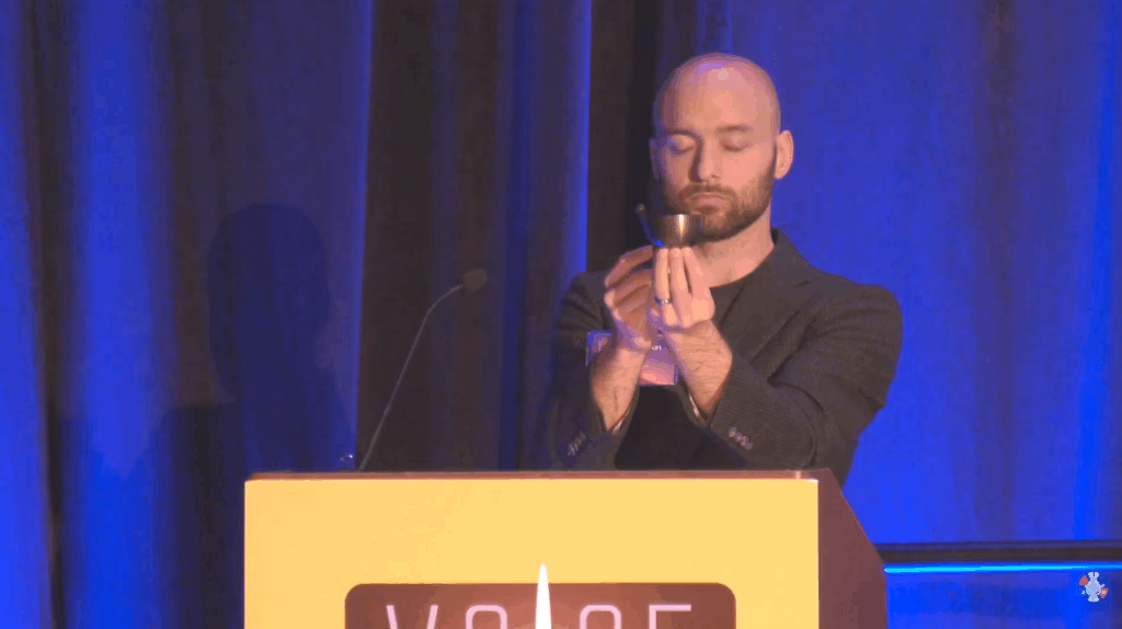 Cameron Conaway at a podium leading a meditation with a small singing bowl.